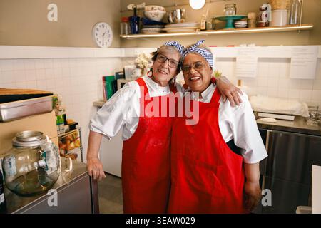 Porträt von zwei glücklichen Seniorinnen, die zusammen in einer professionellen Küche posieren Stockfoto