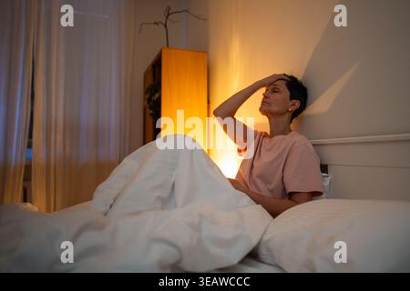 Erschöpfte, nachdenkende Seniorin mit Schlaflosigkeit Schlafstörung im Bett sitzend mit müdem Ausdruck. Stockfoto