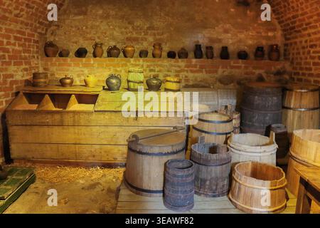 Ein alter, alter Keller mit Ziegelwänden mit einer Vielzahl von Holz- und Tonutensilien, Fässern und Krügen. Stockfoto