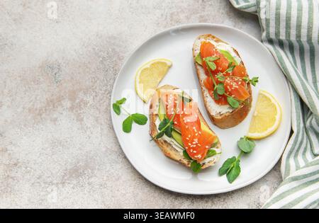 Zwei gesunde Mini-Sandwiches mit Räucherlachs, Avocado, Frischkäse und Erbsensprossen auf einem Teller Stockfoto