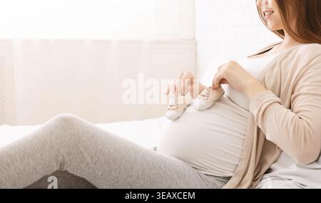 Ich erwarte Freude in einer gemütlichen Umgebung mit Babyschuhen auf einem schwangeren Bauch Stockfoto