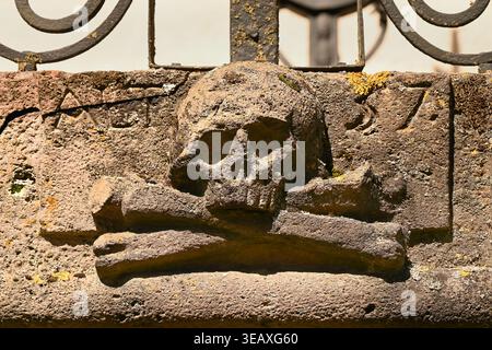 Verwitterter Steinschädel und gekreuzte Knochen Schnitzerei auf historischem Grabstein mit Flechten, in der alten Burg, Banská Štiavnica, Slowakei Stockfoto