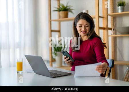 Glückliche lächelnde Frau, die einen Laptop benutzt, hybride Arbeit, online mit einem technischen Gerät zu Hause Stockfoto