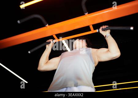 Niedrige Ansicht einer kaukasischen Frau mittleren Alters, die an der Fitnessbar Klimmzüge ausführt und die Kraft und Fitness des Oberkörpers stärkt. Ideal für Workout, Wellness, Trainingsangebote Stockfoto
