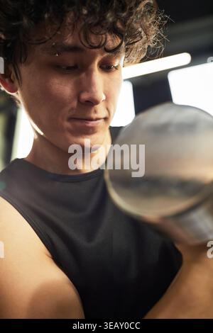 Vertikaler Schuss des jungen erwachsenen Mannes, der Hantel während des Krafttrainings hebt, wobei der Schwerpunkt auf Fitnessfortschritt und gesunde Routine liegt. Geeignet für Sportwerbung, Trainingsanzeigen, Wellness-Kampagnen Stockfoto