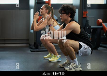 Junge Erwachsene kaukasische Männer und Frauen, die Squat-Übungen im Fitnessstudio, Training der unteren Körperkraft und Fitnessdisziplin durchführen. Nützlich für Trainingsprogramme, persönliches Training, Wellness-Marketing Stockfoto