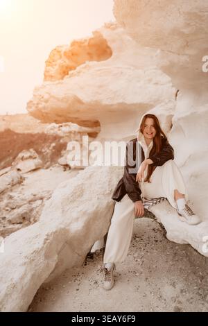 Frau rockt die Natur, die bei Sonnenuntergang auf einer weißen Klippe sitzt, während sie eine schwarze Jacke und einen Kapuzenpullover trägt Stockfoto