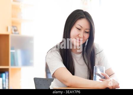 Frau in einem Büro, die Wasser trinkt und glücklich ist Stockfoto