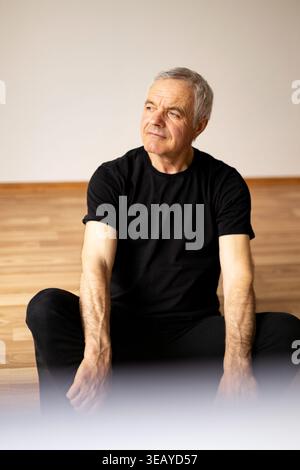 Senior-Mann sitzt auf dem Boden und ruht sich nach dem Yoga-Training aus Stockfoto