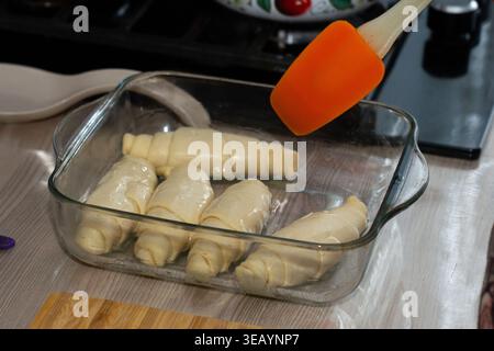 Frisch zubereitete Croissants, gebürstet mit Butter, bereit zum Backen in einer Glasschale an einer Küchenzeile Stockfoto