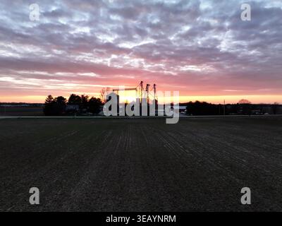 Aus der Vogelperspektive des goldenen Sonnenlichts, das den Horizont über die Silhouetten der Getreideaufzüge und Felder in der Abenddämmerung küsst, Cincinnati, Ohio, USA. Stockfoto