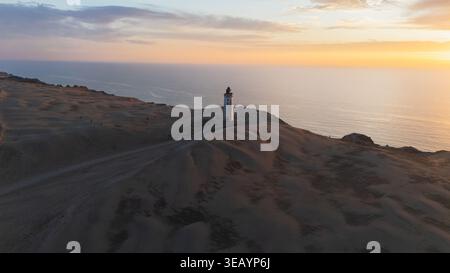 Aus der Vogelperspektive des scharf weißen Leuchtturms, der Wächter vor dem Hintergrund eines feurigen Sonnenuntergangs über der Nordsee steht, Rubjerg Knude Fyr, North Denmar Stockfoto