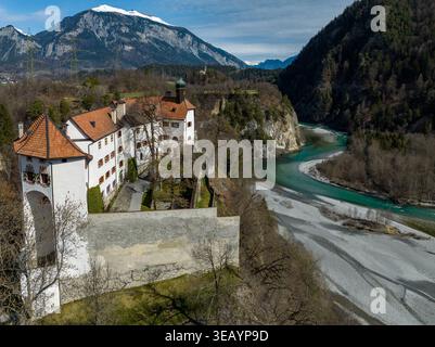 Aus der Vogelperspektive auf das majestätische Schloss Rhäzüns mit seinen roten Ziegeldächern bewacht den türkisfarbenen Rhein vor der Kulisse des schneebedeckten Mo Stockfoto