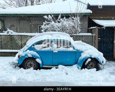 Blauer Oldtimer, der mit Schnee bedeckt ist und in einer Winterstraßenszene geparkt ist. Urbane Umgebung zeigt kaltes Wetter und saisonales Leben. Stockfoto