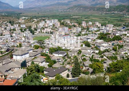 Blick aus einem hohen Winkel auf die historische Stadt Gjirokaster in Albanien mit traditionellen Steindächern und moderner Architektur in einem Bergtal Stockfoto