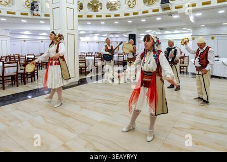 Traditionelle albanische Volksgruppe, die Tanz und Musik in einem Bankettsaal mit Darstellern in ethnischen Kostümen und Instrumenten vorführt Stockfoto