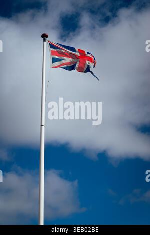 Teilweise zerrissene union-Flagge, die im Wind gegen einen blauen und bewölkten Himmel winkt Stockfoto