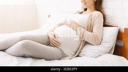 Schwangere Frau, die sich bequem auf einem Bett in einem hellen, gemütlichen Zimmer entspannt Stockfoto