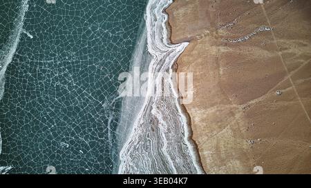 Aus der Vogelperspektive auf dem See mit gefrorenem Ufer und braunem Land. Abstrakter Natur-Hintergrund mit einzigartiger Wintertextur Stockfoto