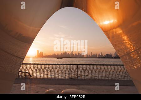 Sonnenuntergang in Dubai, während Sie in der Nähe einer Skulptur am Wasser stehen und die Skyline und die Lichter der Stadt betrachten. Stockfoto