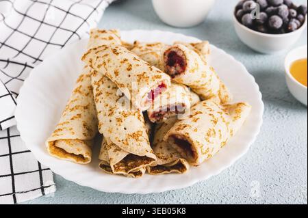 Dünne Pfannkuchen zu Rollen mit Beerenmarmelade auf einem Teller auf dem Tisch Stockfoto