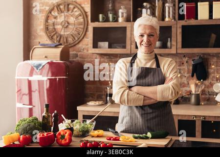 Eine ältere Frau bereitet frisches Gemüse in einer gemütlichen Küche voller natürlichem Licht zu Stockfoto