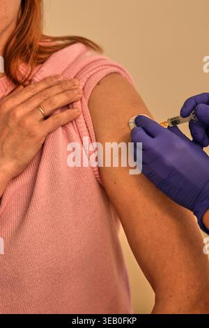 Schwester in blauen Handschuhen, die junge Frau intramuskulär injiziert, Schulterbereich. Stockfoto