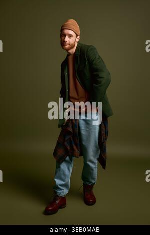 Ein junger Mann im trendigen Outfit posiert vor einem minimalistischen Hintergrund modisch. Stockfoto