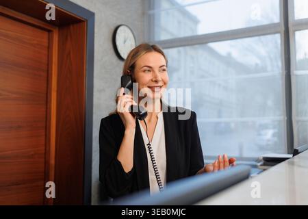 Professionelle Rezeptionistin am Telefon an der Rezeption mit modernem Bürohintergrund Stockfoto