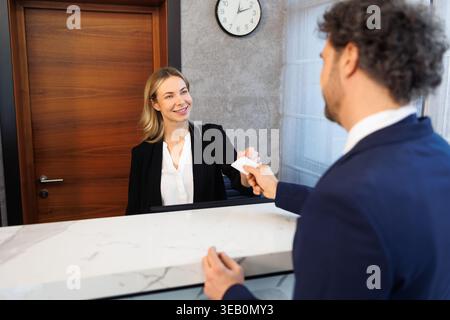Freundliche weibliche Rezeptionistin gibt männlichen Gästen am Schalter des Luxushotels eine Zimmerschlüsselkarte Stockfoto
