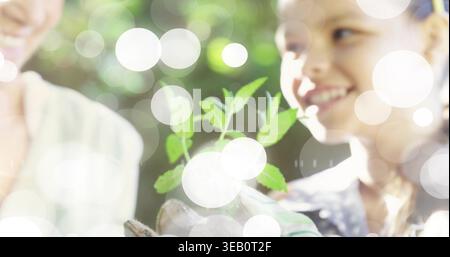 Kleine grüne Sämlinge, ältere Frau und lächelndes Mädchen in Gartenhandschuhen im Garten-Bokeh Stockfoto