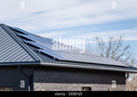 Moderne Photovoltaik-Solarpaneele, die auf einem dunkelgrauen Metall-Stehfalzdach eines privaten Ziegelhauses installiert sind und Lösungen für erneuerbare Energien für SOS zeigen Stockfoto