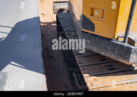 Genaue Details der kontinuierlichen Laufbänder der Erdbewegungsmaschine, die auf Boden in der Nähe von Pflasterflächen für Straßeninstandhaltung und Versorgungsinstallationen im professionellen Einsatz betrieben werden Stockfoto