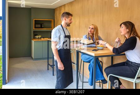 Kellner sprach mit weiblichen Gästen im Café und servierte frische Sandwiches als Vorspeise Stockfoto