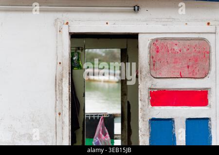 New Taipei City, Taiwan - 1. Februar 2025: Verwitterte Fischerbootttür mit handbemalten roten und blauen Paneelen, die den rustikalen maritimen Charakter widerspiegeln. Stockfoto