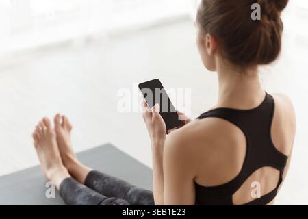 Frau, die im Home Studio in Yoga-Kleidung saß, war mit Smartphone-Aktivitäten beschäftigt Stockfoto