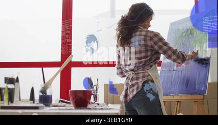 Malerei reifer Künstler, der im Atelier auf Leinwand auf Staffelei arbeitet, kariertes Hemd, Schürze, Kopierraum trägt Stockfoto