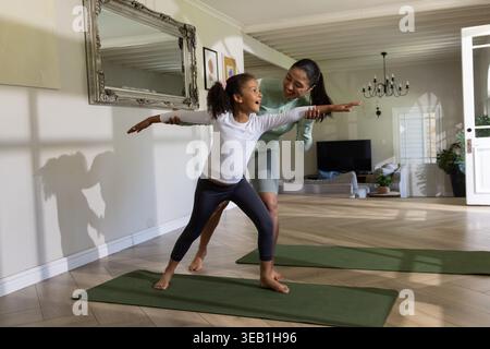 Asiatische Frau, die sanft afroamerikanisches Mädchen führt, das Yoga auf grüner Matte im Wohnzimmer praktiziert Stockfoto