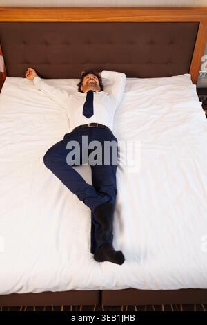 Blick von oben auf Geschäftsmann, der auf einem großen Hotelbett im Anzug schläft oder ausruht Stockfoto