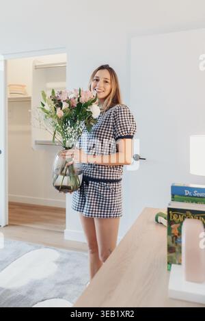 Fröhliche Dame Arrangiert Bright Blossoms. Lächelnde Frau Dekoriert Zu Hause Mit Bunten Blumen. Fröhliche Frau Arrangiert Und Organisiert Farbenfrohe Stockfoto