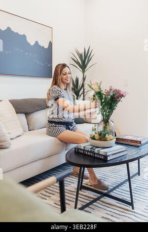 Frau, Die Blumen Auf Couchtisch Platziert. Bezaubernde Blumendekoration In Gemütlichem Wohnbereich. Frische Blüten Auf Dem Zentralen Tisch Arrangieren Stockfoto