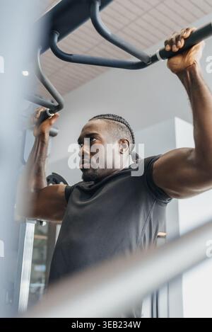 Black Man Trainer Mit Striktem Pullup. Nahaufnahme Des Fokussierten Athleten, Der Overhead Bar Packt, Muskeln Angespannt, Schweiß Auf Der Stirn, Moderner Gym Hintergrund Stockfoto