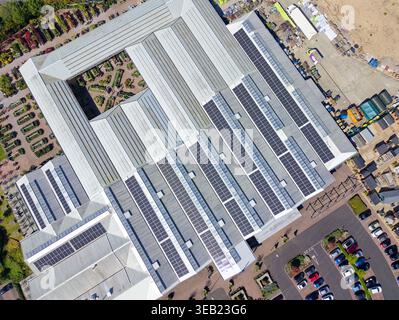Blick aus der Vogelperspektive mit Blick auf Solarpaneele, die auf dem Dach eines großen Gebäudes und Geschäftsgebäudes befestigt sind, um Strom und grüne Energie zu liefern, Großbritannien. Stockfoto