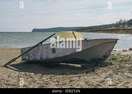 Altes Fischerboot mit Ruder an einem Sandstrand neben dem Meer mit einem hellblauen Himmel, der Einsamkeit und Ruhe repräsentiert Stockfoto