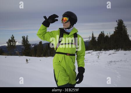 Mann in hellsäuregrünem Snowboardanzug, schwarzen warmen Handschuhen, orangen Brillen, Helm und Rucksack Skier Outfit, reicht Hand in Richtung seines Hades. Erkundet s Stockfoto