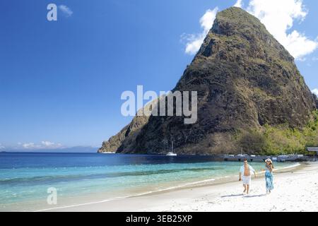 Ein Paar genießt einen gemütlichen Spaziergang entlang des atemberaubenden Strandes in Saint Lucia, umgeben von den majestätischen Pitons vor einem klaren blauen Himmel. Perfekt für ein traumhaftes G Stockfoto