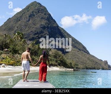 Ein paar spazieren Hand in Hand entlang eines hölzernen Piers, umgeben von der atemberaubenden Schönheit von Saint Lucia Stockfoto