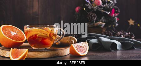 Duftender Tee mit Orangen- und Ingwerstückchen in einer Tasse auf dem Tischbanner Stockfoto