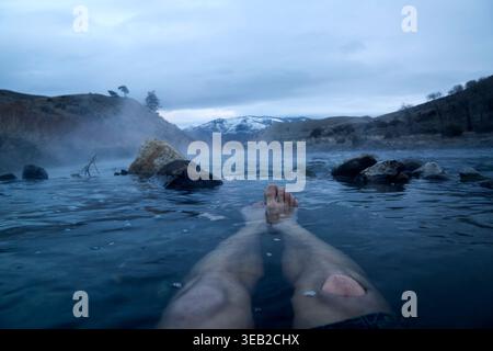 Person, die sich in natürlichen heißen Quellen mit Bergblick entspannt Stockfoto