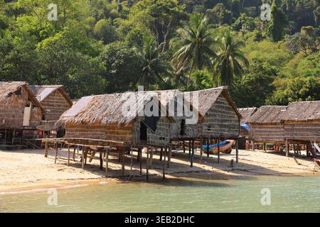 Traditionelle Stelzenhütten säumen einen ruhigen Strand auf den Surin Islands, Thailand, umgeben von üppigen tropischen Wäldern und ruhigem türkisfarbenem Wasser an einem sonnigen Tag. Stockfoto